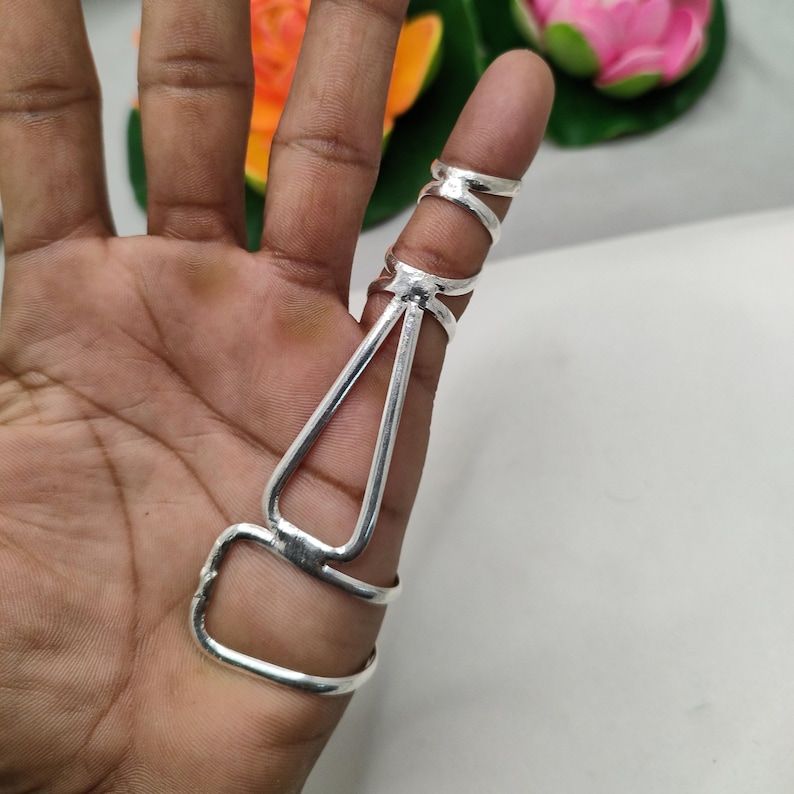 Op de afbeelding: Een zilveren vingerringset. De set bevat een ring voor de basis van de vinger, een ring voor het midden van de vinger en een ring voor de vingertop, verbonden door een decoratief ontwerp.