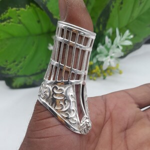 Puede incluir: Un anillo de pulgar de plata con un diseño de jaula y detalles florales intrincados. El anillo tiene una cabeza de león en la parte inferior.