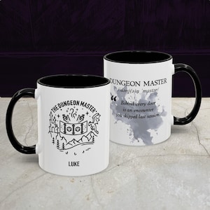 May include: White ceramic mug with a black interior and handle. The mug features the text "DUNGEON MASTER" and a graphic of a castle, dice, and mountains. The name "LUKE" is printed below the graphic. The other side has text about encounters.
