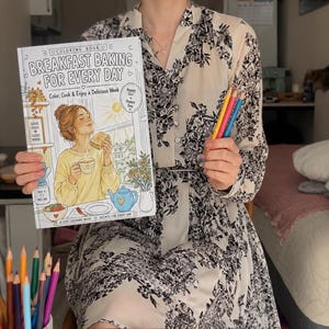 May include: A coloring book titled Breakfast Baking For Every Day featuring a cover illustration of a person with a drink and toast, alongside a separate coloring page titled Tuesday Belgian Waffles with a recipe and a cup of colored pencils.
