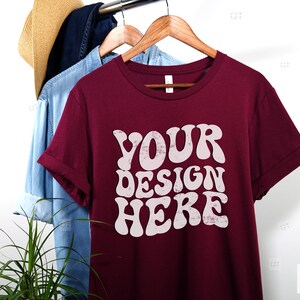 May include: A maroon t-shirt with a white graphic that says "YOUR DESIGN HERE" in a retro, groovy font.