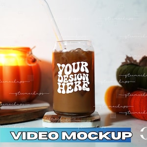 May include: A glass can with a straw filled with iced coffee. The can has a white sticker with the text "YOUR DESIGN HERE" in a retro font. The can is sitting on a wooden coaster on a white surface. There are pumpkins and gourds in the background.