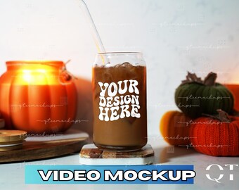 May include: A glass can with a straw filled with iced coffee. The can has a white sticker with the text "YOUR DESIGN HERE" in a retro font. The can is sitting on a wooden coaster on a white surface. There are pumpkins and gourds in the background.