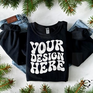 May include: Black long-sleeve sweatshirt with a white graphic that says "YOUR DESIGN HERE" in a retro font. The sweatshirt is laid flat on a white surface with pine branches around it.