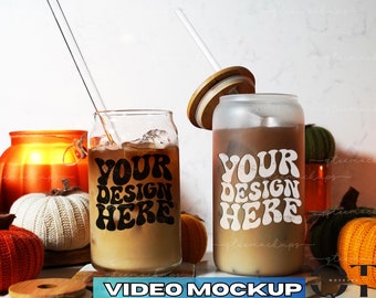 May include: Two clear glass tumblers with lids and straws filled with iced coffee. The tumblers have a white design that says "Your Design Here" in a retro font. The tumblers are surrounded by fall-themed decorations, including pumpkins and gourds.