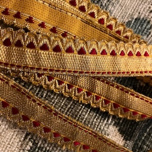 May include: Gold and red trim with a scalloped edge and a repeating heart pattern.