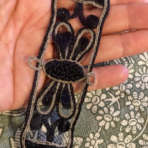 May include: Black and silver embroidered trim featuring a floral design. The trim is made from a soft, silky fabric and has a delicate, intricate pattern.