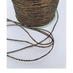 May include: A spool of black and gold cord. The cord is thin and has a subtle shimmer.