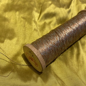 May include: A spool of metallic thread with a wooden base. The thread is a mix of silver and copper colors. The spool is labeled "Col. 6".