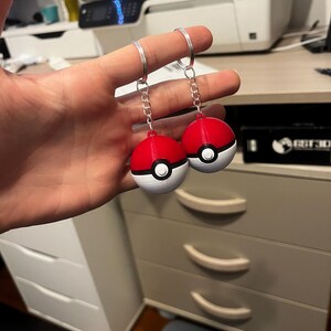 Può includere: Due Poké Ball rosse e bianche su portachiavi. Le Poké Ball sono stampate in 3D e hanno un contorno nero attorno al cerchio bianco.