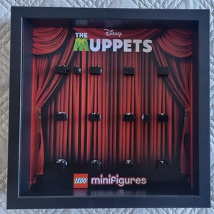 May include: A black frame with a red curtain backdrop featuring the text "The Muppets" and the Disney logo. The frame has 10 empty slots for LEGO minifigures and the text "LEGO minifigures" at the bottom.
