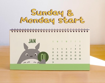 May include: A spiral-bound desk calendar featuring a gray cartoon creature illustration for January. The page displays the text Sunday & Monday start, the month JAN, and a grid of dates. The design includes a green horizontal band at the bottom.