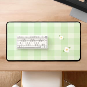 Op de afbeelding: Een groene en witte geruite bureaumat met een wit toetsenbord en twee witte bloemen met groene stelen.