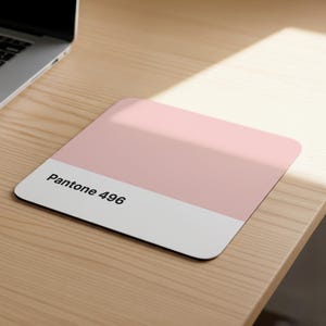 Può includere: Un tappetino per mouse rettangolare con un design a due toni. La parte superiore è rosa chiaro uniforme e la parte inferiore è bianca. Il testo "Pantone 496" è stampato in nero sulla sezione bianca. Il tappetino è su una superficie di legno chiaro.