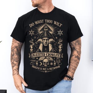 Könnte beinhalten: Schwarzes T-Shirt mit einem Aufdruck mit dem Text „DO WHAT THOU WILT“ über einer Illustration von Aleister Crowley. Das Design umfasst eine Pyramide mit einem Auge, Sterne, Kerzen, einen Totenkopf und den Satz „MAGICK IS NOT A METAPHOR“.