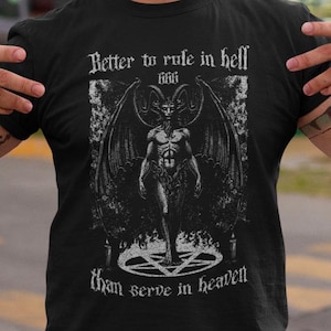 Op de afbeelding: Een zwart T-shirt met een witte grafische print van een gevleugelde demon die op een pentagram staat. De tekst op het shirt luidt "Better to rule in hell 666 than serve in heaven".