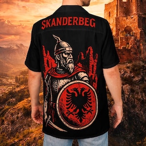 Puede incluir: Camisa negra con botones con un gráfico de Skanderbeg, una figura histórica, con un escudo rojo y el texto "SKANDERBEG" en la espalda. El diseño está ambientado en un castillo y una bandera.
