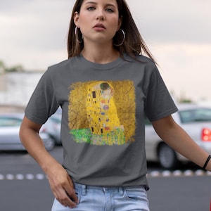 Distressed style t-shirt featuring Gustav Klimt painting The Kiss, rendered in faded gold and black tones on soft, white cotton fabric, suitable for art lovers.