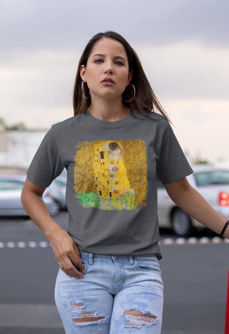 Distressed style t-shirt featuring Gustav Klimt painting The Kiss, rendered in faded gold and black tones on soft, white cotton fabric, suitable for art lovers.