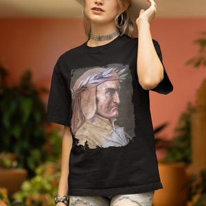 Könnte beinhalten: Eine Frau trägt ein schwarzes T-Shirt mit einem Porträt eines Mannes mit einem Lorbeerkranz auf dem Kopf. Das T-Shirt hat einen Used-Look. Die Frau trägt außerdem einen weißen Hut, Jeans-Shorts und silbernen Schmuck.