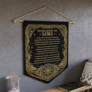 May include: Black banner with gold text and illustrations. The banner reads "Invocation to Loki" and includes a poem. The bottom of the banner features a Viking compass design. The banner is hung from a wooden rod with a string.