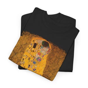Distressed style t-shirt featuring Gustav Klimt painting The Kiss, rendered in faded gold and black tones on soft, white cotton fabric, suitable for art lovers.