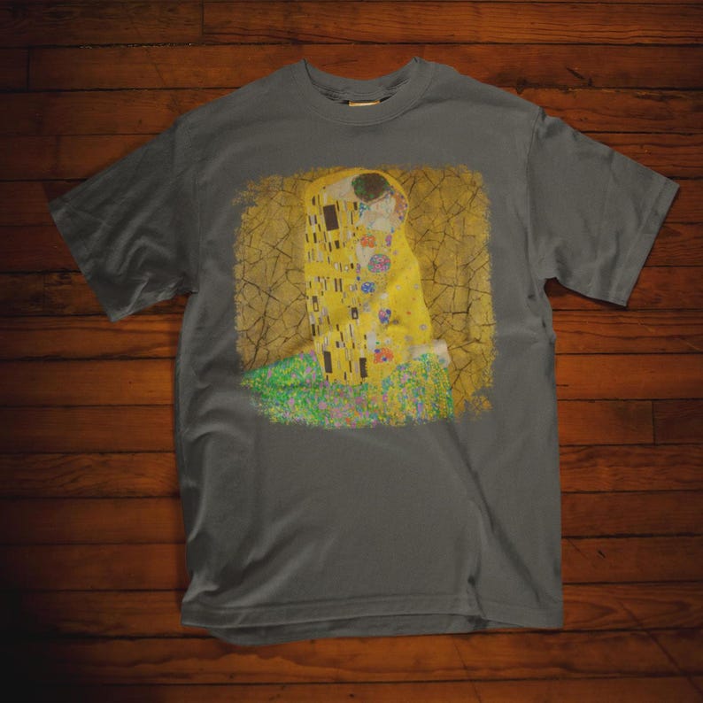 Distressed style t-shirt featuring Gustav Klimt painting The Kiss, rendered in faded gold and black tones on soft, white cotton fabric, suitable for art lovers.