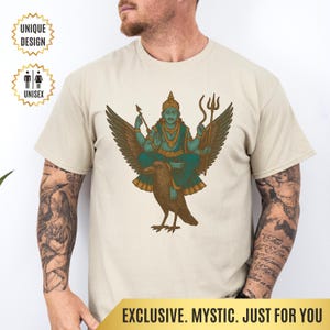 Puede incluir: Camiseta unisex beige con una ilustración turquesa y marrón de una deidad montada en un cuervo. El diseño incluye un tridente y arco y flecha. La camiseta tiene el texto "UNIQUE DESIGN" y "UNISEX". La parte inferior de la camiseta tiene el texto "EXCLUSIVE. MYSTIC. JUST FOR YOU."