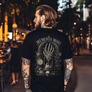 Memento Mori shirt featuring a vintage skeleton hand holding an hourglass, inspired by Stoic philosophy and mortality symbolism. Gothic t-shirt design with dark academia aesthetic, antique engraving style artwork, and memento mori theme. Perfect for lovers of stoicism, philosophy, gothic fashion, medieval art, existential symbolism, and alternative clothing.