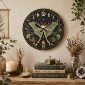 May include: A round wall clock featuring a large pale green moth at its center, surrounded by a dark background with gold Roman numerals, botanical illustrations, and lunar phases. The clock has two black hands and a circular frame.