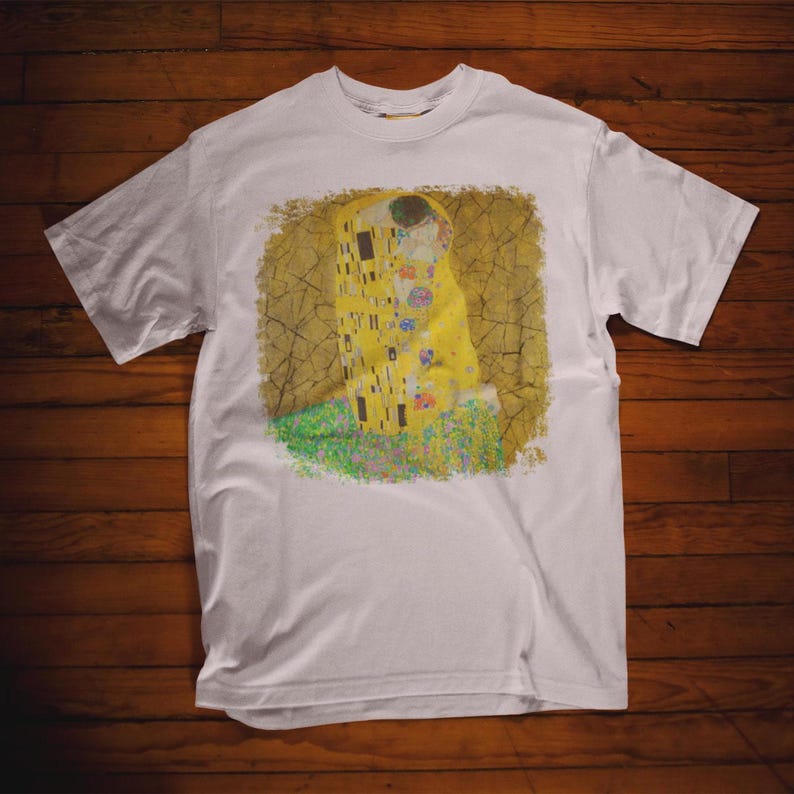 Distressed style t-shirt featuring Gustav Klimt painting The Kiss, rendered in faded gold and black tones on soft, white cotton fabric, suitable for art lovers.
