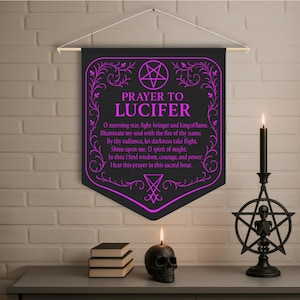 May include: Black banner with the text "PRAYER TO LUCIFER" in purple, along with a prayer. The banner is hanging above a table with a skull candle, books, and a black candle holder with a skeleton inside a pentagram.