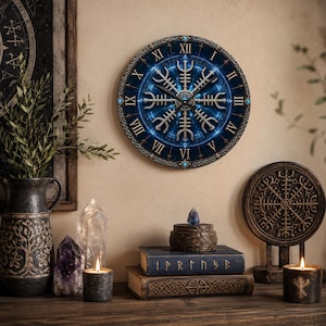 Puede incluir: Un reloj de pared circular con fondo azul, un símbolo Vegvisir plateado, números romanos y pequeños detalles azules. La esfera muestra un diseño celestial detallado y brillante en tonos azul oscuro con manecillas plateadas.