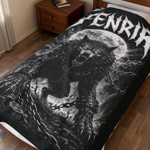 Op de afbeelding: Zwart-wittekening van een grommende wolf in ketens, tegen een volle maan. Het woord "FENRIR" staat in witte letters. De deken ligt op een bed.