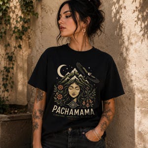 May include: A black short-sleeve t-shirt featuring a graphic print of a face surrounded by mountains, a crescent moon, an eagle, and flowers. The text PACHAMAMA is printed in large letters, with the words NURTURE, ABUNDANCE, BALANCE printed below.