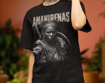Può includere: T-shirt nera con una grafica dettagliata di una guerriera e la scritta "AMANIRENAS". La guerriera è raffigurata con uno scudo, una lancia e immagini di leoni, in un carattere invecchiato, creando un design sorprendente.