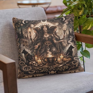 May include: Square decorative pillow featuring a mystical illustration. The artwork depicts three women, candles, a cauldron, and a black dog. The color palette includes shades of brown, black, and gold, creating a vintage aesthetic. The pillow is placed on a gray chair.