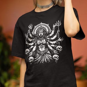 May include: Black t-shirt featuring a white graphic print of a multi-armed deity with skulls and a trident.