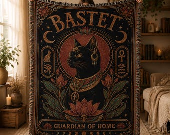 May include: A black woven throw blanket featuring a central illustration of a black cat adorned with gold jewelry, surrounded by lotus flowers, Egyptian symbols, and the text BASTET and GUARDIAN OF HOME, finished with a decorative fringed edge.