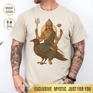 May include: Beige unisex t-shirt featuring a detailed illustration of a deity seated on a large bird, holding various symbolic objects. The design includes a golden halo and is labeled "UNIQUE DESIGN" and "UNISEX". The bottom banner reads "EXCLUSIVE. MYSTIC. JUST FOR YOU."