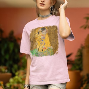 Distressed style t-shirt featuring Gustav Klimt painting The Kiss, rendered in faded gold and black tones on soft, white cotton fabric, suitable for art lovers.