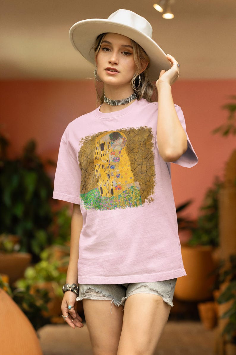 Distressed style t-shirt featuring Gustav Klimt painting The Kiss, rendered in faded gold and black tones on soft, white cotton fabric, suitable for art lovers.