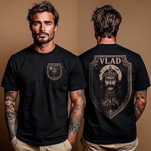May include: Black t-shirt featuring a graphic of Vlad the Impaler on the front and back. The front graphic is a small shield with the word "VLAD" above a portrait. The back graphic is a larger shield with the word "VLAD" and a portrait of Vlad.