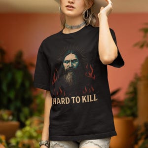 May include: Black t-shirt with a graphic of a man with a beard and flames. The text "Hard to Kill" is printed below the graphiMystical Rasputin t-shirt featuring a dark grunge occult illustration inspired by the legendary Russian mystic, with gothic aesthetic and esoteric symbolism. Funny dark humor shirt for history lovers, occult fans, and gothic style enthusiasts, designed with a vintage distressed look.c.