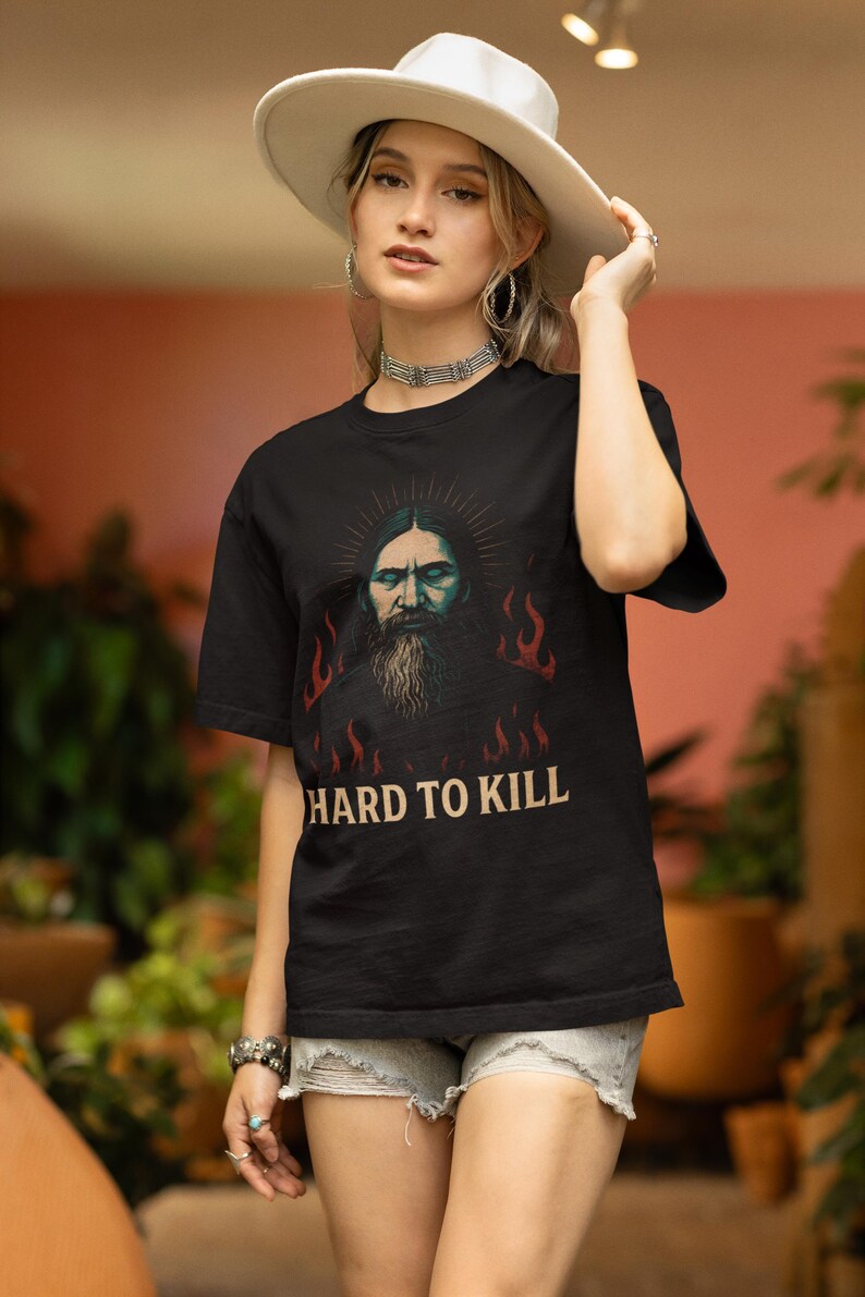 May include: Black t-shirt with a graphic of a man with a beard and flames. The text "Hard to Kill" is printed below the graphiMystical Rasputin t-shirt featuring a dark grunge occult illustration inspired by the legendary Russian mystic, with gothic aesthetic and esoteric symbolism. Funny dark humor shirt for history lovers, occult fans, and gothic style enthusiasts, designed with a vintage distressed look.c.