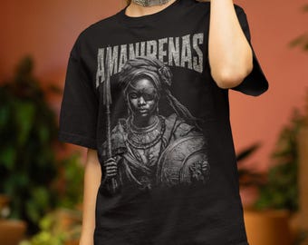 Può includere: T-shirt nero con un'illustrazione in scala di grigi di una guerriera che tiene una lancia e uno scudo. Il testo "AMANIRENAS" è stampato in alto con un carattere invecchiato. La guerriera indossa gioielli e un copricapo.
