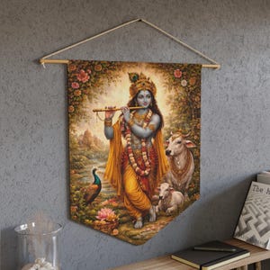 Può includere: Un arazzo da parete con un'illustrazione dettagliata di una divinità che suona il flauto, circondata da un pavone, mucche e un fogliame lussureggiante. L'opera d'arte è prevalentemente dai toni caldi, con sfumature dorate, arancioni e verdi. Lo stendardo è sospeso da un'asta di legno.