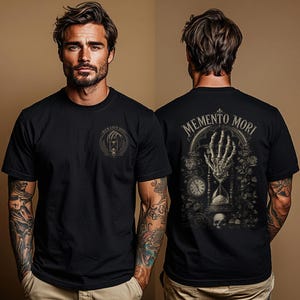 May include: A black short-sleeve t-shirt featuring a small circular graphic on the front chest with the text Memento Mori. The back displays a large detailed illustration of a skeletal hand holding an hourglass, a clock, and roses with the text Memento Mori.