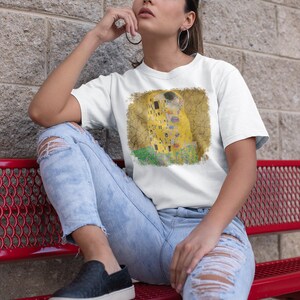 Distressed style t-shirt featuring Gustav Klimt painting The Kiss, rendered in faded gold and black tones on soft, white cotton fabric, suitable for art lovers.