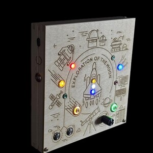 May include: Wooden box with an engraved space exploration theme. The box features a central rocket design, the text "EXPLORATION OF THE MOON", and various illuminated LED lights. Includes a knob and several buttons.